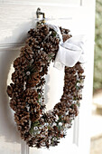 A detail of a Christmas wreath tied with a white ribbon to an open front door