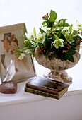 Close up detail of a stone vase of holly and ivy next to a framed picture and two vintage books