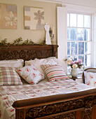 A traditional bedroom with two canvas paintings above an ornate wooden bed with floral bed linen
