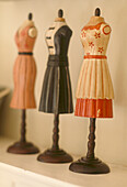 Close up detail of three ornaments of mannequin dummies dresses with wooden bases on a shelf