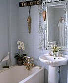 Traditionelles Badezimmer mit großem Silberrahmenspiegel über einem Waschbecken daneben Badewanne mit goldenen Wasserhähnen und Duscharmaturen