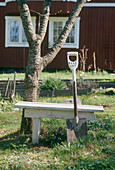 Spade propped up against a white bench next to a tree