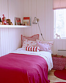 A child's bedroom done in bright fuchsia and white colours with a bed and toys on a shelve