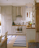 Detail of a traditional kitchen with blue and white striped rugs on the floor below oak kitchen units