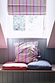 Window seat with painted panelling and candy stripe cushion and roman blind