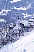 Blick von oben auf ein schweizer Dorf und eine Kirche in den schneebedeckten Bergen