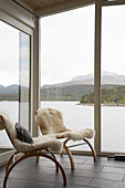 Pair of wooden chairs with furry covers in window overlooking lake