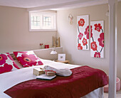 Doppelbett mit rotem Überwurf, Kissen mit roten Blumenmotiv und passenden Wandbildern