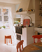 Country style kitchen with a stove surrounded by white tiles next to a small red stool