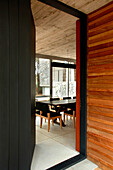 Black front door opens onto modern kitchen dining area of a woodland house with Lapacho wood and black painted cladding