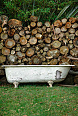 Vintage-Badewanne im Garten vor Stapel mit Brennholz
