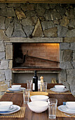 Grill set in exposed stone wall with wooden table and place settings