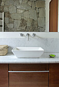 Drawer unit below bathroom sink with large mirror reflecting exposed stone wall