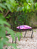 Schmiedeeiserner Stuhl mit rosa Blumenmuster auf einer Kiesterrasse