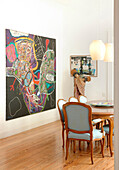 Lit pendant lights and oversized artwork in dining room with wooden floor