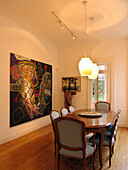 Lit pendant lights over wooden dining room table with art work from Brazil