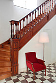 Red velvet armchair on chequered floor under wooden staircase
