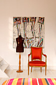 Modern art above red upholstered armchair and mannequin in child's room with striped bed cover
