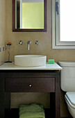 Ceramic basin set on dark wood wash stand below mirror