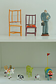 Dolls house chairs and cow statuettes on white shelving unit