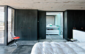 En suite bathroom in bedroom with cedar wardrobes a concrete floor and a Jacobsen chair