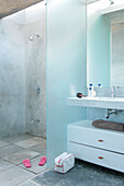 Badezimmer mit abgeschirmtem Waschbecken aus Carrara-Marmor und eingebettetem Spiegel über MDF-Schrank und Duschboden mit Betonfertigteilfliesen, die den Wasserabfluss ermöglichen