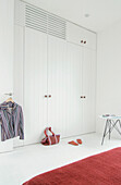Striped shirt hangs on panelled wardrobe door with shopping bag and Indian slippers
