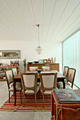 Pendant light hangs from panelled ceiling above dining table on striped rug