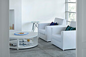 Weißes Wohnzimmer mit gepolsterten Sesseln und rundem Couchtisch