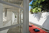 Floor cushions set on rug and view through window to concrete beach house corridor