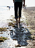 rear view of man walking barefoot along beach