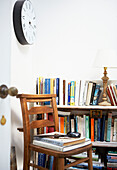 Wooden chair under clock with bookcase