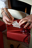 Woman writing gift tag on Christmas presents wrapped with ribbon