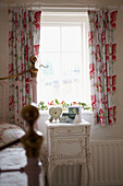 Floral pattern curtains above white pained bedside table