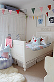 Kinderzimmer mit Wimpeln und Sternenkissen, weiß gestrichenen Möbeln und gerahmter Babykleidung