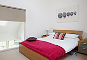 Rosa Decke auf einem Doppelbett in einem Öko-Haus mit großen verglasten Fenstern, durch die die Sonne das Gebäude aufheizt