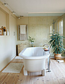 Freistehende Badewanne in einem sonnendurchfluteten Badezimmer mit Holzboden und Glasduschabtrennung