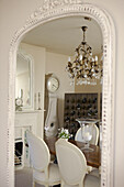 Crystal drop chandelier and dining room reflected in oversized mirror with painted frame