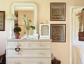 Framed tapestry beside painted chest of drawers with mirror