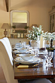 Place settings with white flower arrangements on wooden dining room table