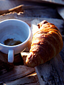 Sonnenbeschienenes Croissant und leere Kaffeetasse