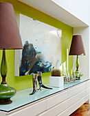 Matching lamps with brown shades set against lime green feature wall with modern art canvas