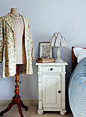 Floral coat on mannequin's dummy next to painted bedside cabinet