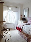 Sonnendurchflutetes Schlafzimmer im Landhausstil mit gestepptem Bettbezug und herzförmigem Kissen auf einem Klappstuhl