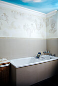 Cherub wallpaper and fresco of sky above bath with wire rack