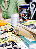 Woman sits with needlecraft books and a jar of buttons with fabric