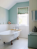 Freestanding rolltop bath in pastel green bathroom with tongue and groove panelling