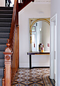 Arched mirror in tiled hallway with wooden banister of London home