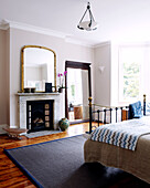 Full length mirror next to fireplace in London bedroom with polished wooden floor
