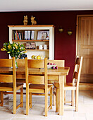 Dining room table and chairs with dark red walls and bookcase